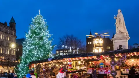A large lit-up Christmas tree sits within a brightly lit market