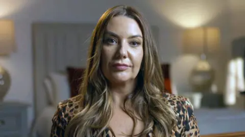 Photo of Lisa looking directly at the camera. She has long brown hair and is wearing a top with a leopard-skin pattern. The background is blurred but appears to be a living room.