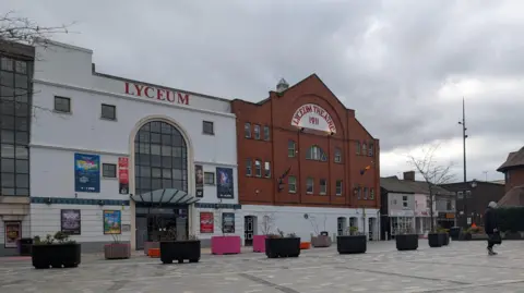The Lyceum Theatre in Crewe, a mainly white-coloured building with part of it red brick. The theatre stands in a paved area.
