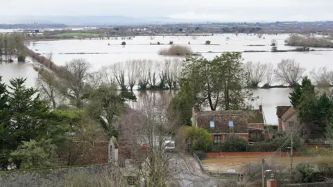 PA Media An aerial shot of flooding on the Levels. There are homes in the background and a large number of flooded fields in the background, with trees bordering the fields.