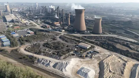 Getty Images An aerial view of the British Steel site in Scunthorpe. There is an array of chimney structures, with steam billowing out of cooling towers, two in the foreground and two in the background. There are numerous sheds and containers, along with piles of materials.