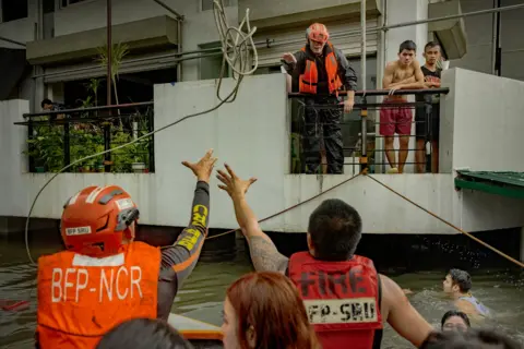 Ezra Acayan/Getty Images Rescuers reach for a rope as they ride a boat to reach residents trapped by flooding caused by Typhoon Gaime and monsoon rains on July 24, 2024 in Quezon City, Metro Manila, Philippines.