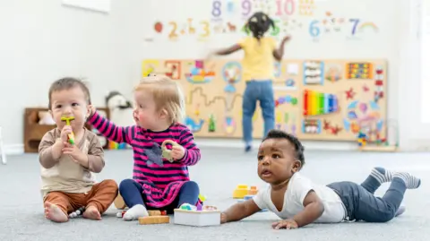 Getty Images A small group of toddlers sit on the floor of a daycare room 