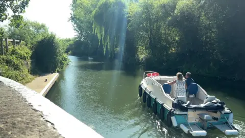 People on a boat on the water travelling down the river into the sun, flanked by trees