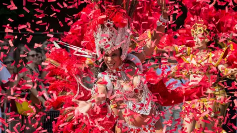 Dancer in elaborate, brightly coloured feathered costume takes part in a vibrant street parade during Notting Hill Carnival.