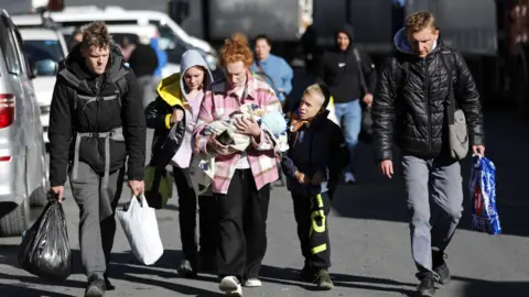 Getty Images Young man, a woman with a baby and children walk to cross the border from Russia into Georgia. Photo: 27 September 2022