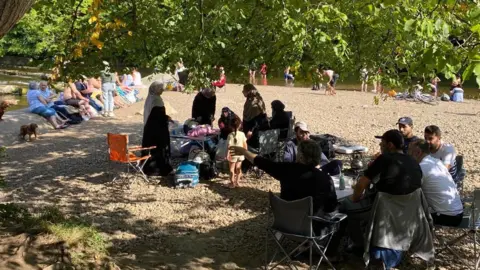 Save Our Swale About thirty people enjoying the site at Richmond Falls. Some are dipping their toes in the water, while others are socialising on the rocks or around folding tables and chairs. 