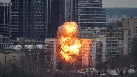 A large explosion and orange fireball rises from an apartment block