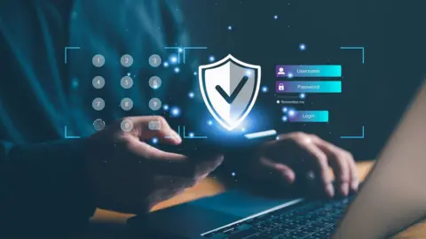 Getty Images A man using a mobile phone and laptop with graphics showing a shield