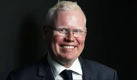 ABC News/Justin Huntsdale Gareth Ward, smiling at camera, wearing a dark suit and tie and glasses