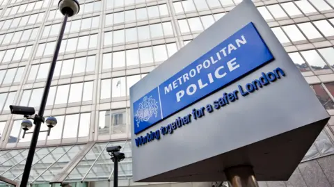 The well-known triangular Metropolitan Police sign is in the foreground of the image with the police headquarters in the background