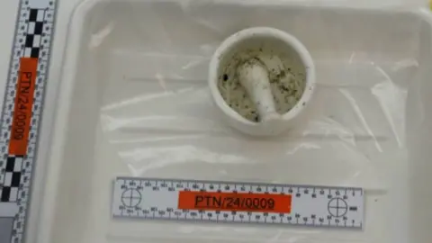 Merseyside Police Picture of a white pestle and mortar with dark ground material, in a white plastic evidence tray, positioned next to a ruler to indicate its size.