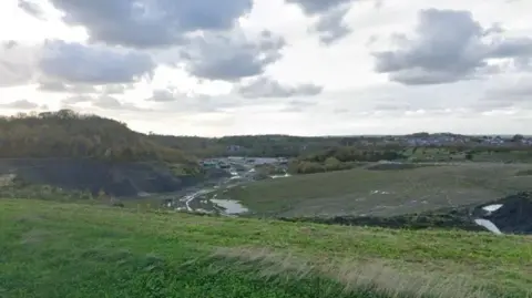 Google A wide view of the site showing undulating grassland and housing in the distance