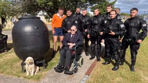 Royal Navy War veteran Boyd Salmon sits in a wheelchair at the Royal Navy's Portsmouth base surrounded by eight members of the navy's current diving team