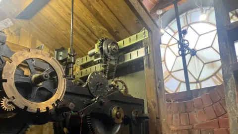 Elizabeth Baines/BBC Cogs in the tower behind the clock face.