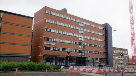 The Salvation Army Six-storey, red brick building, with sign reading William Booth Centre on the left-hand side. Roadworks with cones and fencing taking place in-front of the building.