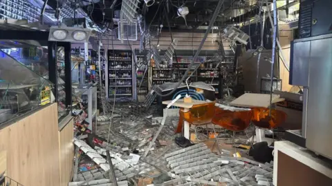 DSNS The inside of a petrol station is destroyed by a Russian attack. Wires hang from the roof and shelves and debris are strewn all over the floor 