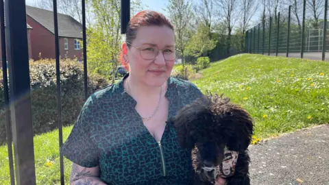 Jayne is pictured wearing a green and black shirt, holding a dog