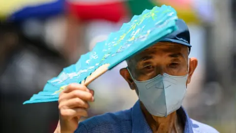 A man wearing a mask uses his fan to shade himself from the sun during a heatwave in Seoul 