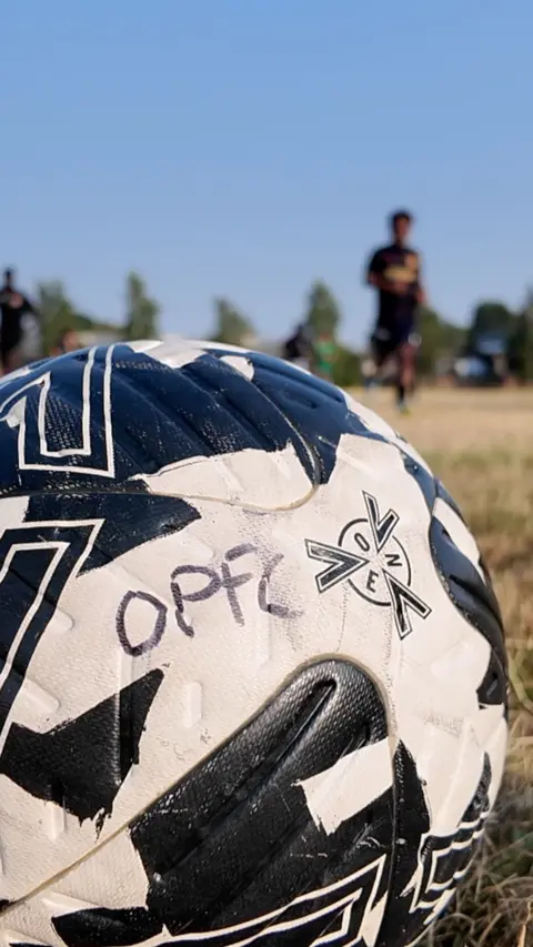 A football with OPFC written on it against a blue sky.