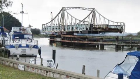 Reedham swing bridge open for river traffic. Blue and white boats are moored on the river bank