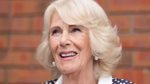 Camilla smiles in front of a red brick wall.