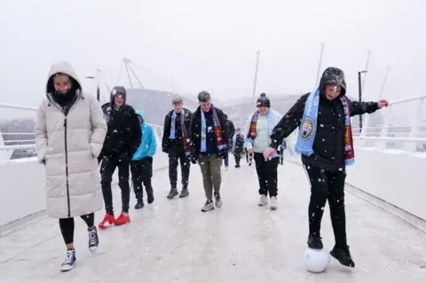 Martin Rickett/PA Media Fans cross the bridge to the stadium in the snow before the Premier League match at the Etihad Stadium, Manchester.