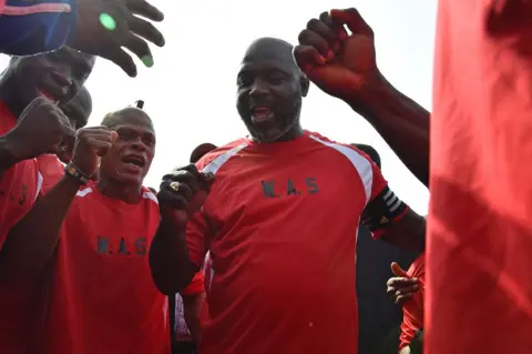 AFP Liberia's president-elect and former football star George Weah (C) reacts with teammates prior to taking part in a friendly football match between Weah All Stars team and Armed Forces of Liberia team