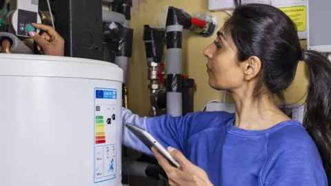 Getty Images A woman adjusts her thermostat at home