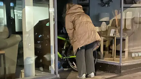 Daisy and Emma are speaking to a couple bedded down beside a bicycle in a shopfront