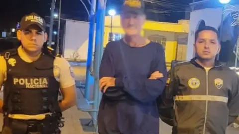 Ecuadorian Police Blurred Mr Armstrong stood between two stern-faced police officers.