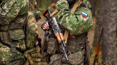 A Russian soldier in fatigues adorned with a patch of the country's flag holds  a  machine gun