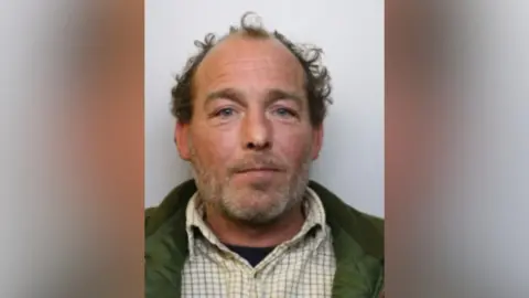 Avon and Somerset Police Trevor Nex is looking at the camera wearing a green coat and a chequered shirt.