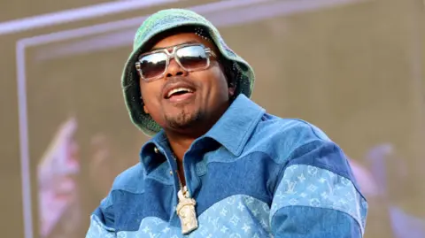 Getty Images US rapper Nas wearing sunglasses and a hat smiles on stage in a blue shirt 