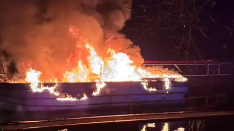 North Wales Fire Service A pleasure boat on water in flames in the dark