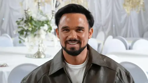 Shaun Whitmore/BBC Head and shoulders image of Gareth Gates in a room with white tablecloths, white chairs and white sheets on the wall. He has short brown hair, beard and moustache, and is wearing a white T-shirt and a brown jacket. 