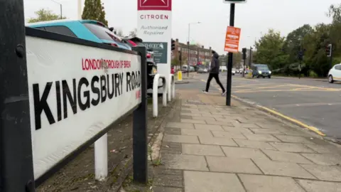 BBC Kingsbury Road road sign and a pedestrian crossing the road