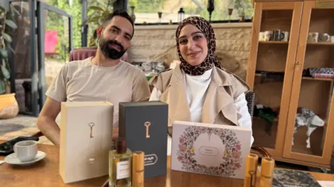 Sebastian Usher Qassem Abu Khalaf and his wife Malak Hijaz with a bunch of their perfumes on a wooden table.