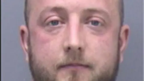 A very close-up custody picture showing a man with a blonde beard and blue eyes