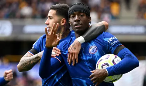 Getty Images Noni Madueke holding the ball and holding up three fingers to mark his hattrick on Sunday