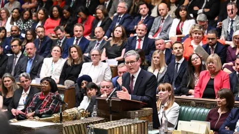 UK Parliament A wide shot of the Labour benches in the Commons chamber, with Sir Keir Starmer speaking at the despatch box and the Parliament mace and Erskine May books in the foreground