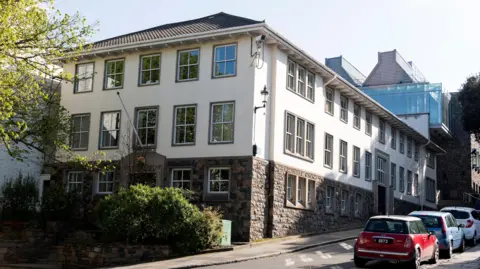 The Law Offices of the Crown, St. James Chambers in St. Peter Port, Guernsey in the Channel Islands, Britain. It is a building with a brick bottom and a cream top covred in rectangular windows. 