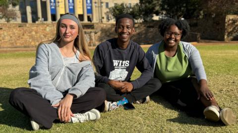 Three students sit on a university lawn 