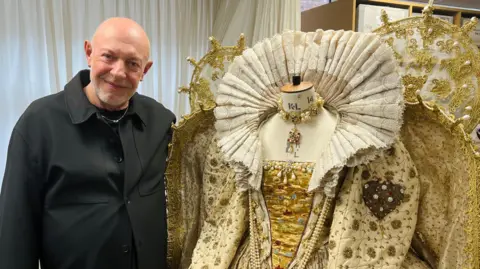 Stephen Rodwell stood next to an Elizabethan era dress which is cream coloured.