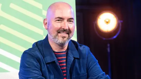 Getty Images Scottish-American writer and fashion designer Douglas Stuart attends the Edinburgh International Book Festival at Edinburgh College of Art on August 28, 2022 in Edinburgh, Scotland. He is waring a blue and red stripey T-shirt and a blue jacket.