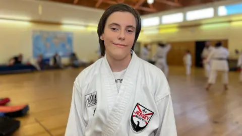Grace Greenwood smiles at the camera in front of karate class while wearing her Jersey Wado Ryu gi