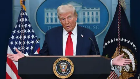 Getty Images Donald Trump giving White House briefing on 30 January about the air collision in Washington. He is mid-speech, with his hands raised on either side of the lectern he is standing behind. He is wearing a navy blazer, white shirt and red tie.