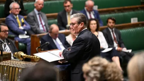 Reuters Keir Starmer, who has grey gelled hair and wears black glasses, speaks at the despatch box in the Commons as MPs look on