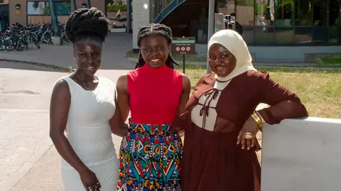 Francisca Arhinful, Jemimah Mensah and Fadila Issah, lined up together and smiling broadly. They are standing outside Cambridge University's Faculty of Education. 