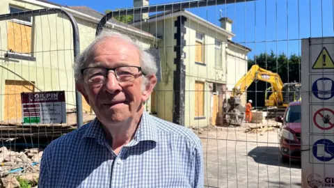 Alan Tyerman, cabinet member for housing and finance at Torbay Council, in a blue and white check shirt in front of the demolition site